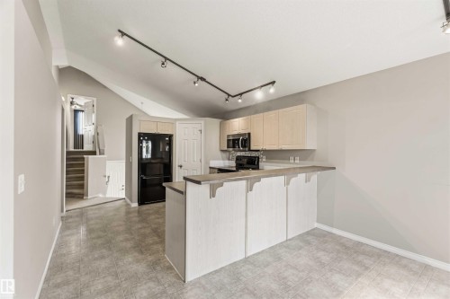 Kitchen featuring black appliances, light wood-finish cabinetry, and a breakfast bar - 2012 35A Avenue, Edmonton, AB 