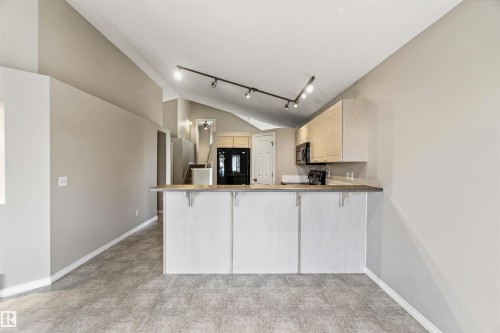 Open-concept kitchen area featuring a breakfast bar with a light wood-finish countertop, light wood cabinetry, and track lighting - 2012 35A Avenue, Edmonton, AB 