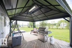 Expansive outdoor deck featuring wood-finish flooring, a metal-framed gazebo with a pitched roof, and an overhead light fixture - 
