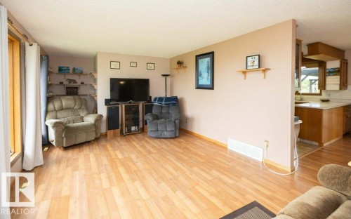 Spacious living area featuring wood-finish flooring, ample natural light from a large window, a partial wall separating it from a kitchen area, and built-in wall shelving - 57532 Rg Rd 270, Rural Westlock County, AB 