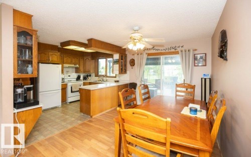 Open-concept kitchen and dining area featuring wood-finish flooring, oak cabinetry, white appliances, and a sliding glass door leading to an outdoor space - 57532 Rg Rd 270, Rural Westlock County, AB 