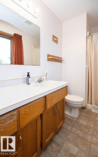Bathroom featuring a wood-finish vanity with a white countertop and integrated sink, a large wall-mounted mirror, and patterned floor tiles - 57532 Rg Rd 270, Rural Westlock County, AB 