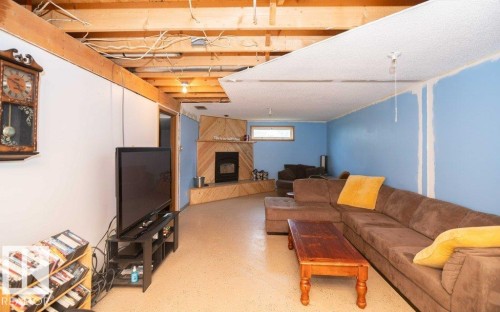 Lower-level room featuring a corner-set fireplace with a wood-finish surround, exposed ceiling joists with wiring, light blue painted walls, partially finished ceiling, and light-toned flooring - 57532 Rg Rd 270, Rural Westlock County, AB 