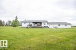 Expansive green lawn with a white exterior home featuring a rear deck and mature trees - 