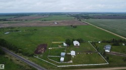 Expansive rural property featuring a primary residence with a gray roof, multiple outbuildings, and a white perimeter fence - 