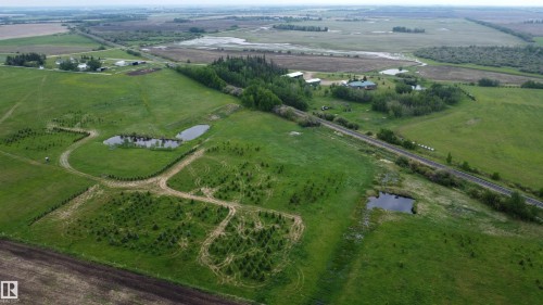 Expansive green landscape featuring multiple ponds, a residential structure with green roofing, a treeline, and a railroad track - 57532 Rg Rd 270, Rural Westlock County, AB 