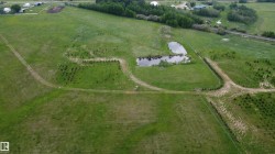 Expansive green acreage featuring a natural pond, established treelines, and visible vehicle paths - 