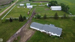 Expansive rural property featuring multiple outbuildings, a white perimeter fence, and a substantial main building with a gray shingle roof - 