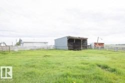 Expansive green field featuring a large open-sided shed with a corrugated metal roof and siding, a white outbuilding with a metal roof, and perimeter fencing - 