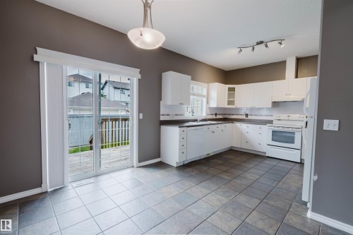 Kitchen and dining area featuring white cabinetry and appliances, tile flooring, track lighting, and a suspended ceiling light - 38 1780 Glastonbury Boulevard, Edmonton, AB 