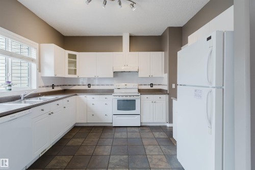 Kitchen featuring white cabinetry, a double basin stainless steel sink, a dishwasher, a white oven/range, and tile flooring - 38 1780 Glastonbury Boulevard, Edmonton, AB 