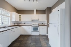 Kitchen featuring white cabinetry, a double basin stainless steel sink, a dishwasher, a white oven/range, and tile flooring - 