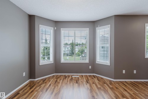 Room featuring a bay window with three individual sashes, wood-finish flooring, and light gray wall paint - 38 1780 Glastonbury Boulevard, Edmonton, AB 