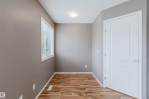 Room featuring wood-finish flooring, a white trim window with blinds, and a white panel door - 38 1780 Glastonbury Boulevard, Edmonton, AB 