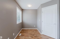 Room featuring wood-finish flooring, a white trim window with blinds, and a white panel door - 