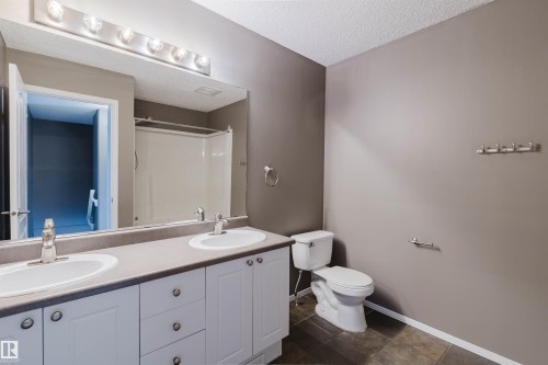 Bathroom featuring a dual vanity with white cabinetry, a single toilet, and a combination tub/shower unit - 38 1780 Glastonbury Boulevard, Edmonton, AB 