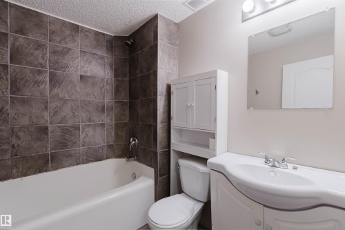 Full bathroom featuring a white tub, dark-toned square wall tiles, a classic white vanity with an integrated sink, and an overhead medicine cabinet - 38 1780 Glastonbury Boulevard, Edmonton, AB 