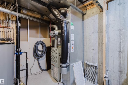 Utility room featuring a forced-air furnace, exposed ductwork, concrete foundation walls, and a hot water heater - 38 1780 Glastonbury Boulevard, Edmonton, AB 
