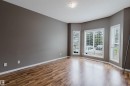 Spacious room featuring wood-finish flooring, a contemporary ceiling light fixture, and a bay window configuration with white window blinds - 38 1780 Glastonbury Boulevard, Edmonton, AB 