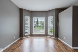 Bay window feature with three vertical windows and white blinds, complemented by wood-finish flooring, neutral gray walls, and white baseboards - 