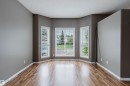 Bay window feature with three vertical windows and white blinds, complemented by wood-finish flooring, neutral gray walls, and white baseboards - 38 1780 Glastonbury Boulevard, Edmonton, AB 