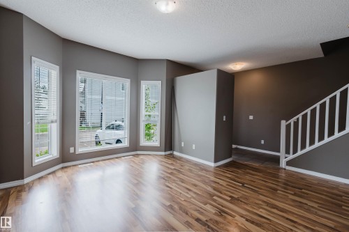 Spacious living area featuring wood-finish flooring, a contemporary gray wall color, and multiple windows with white blinds - 38 1780 Glastonbury Boulevard, Edmonton, AB 