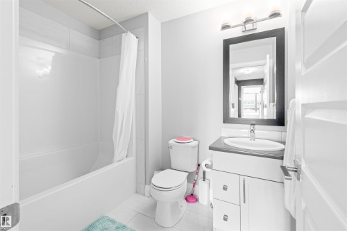 Bathroom featuring a tub/shower combination with white subway tile surround, white vanity with a dark countertop, undermount sink, and a framed mirror with integrated lighting - 389 Charlesworth Drive, Edmonton, AB 
