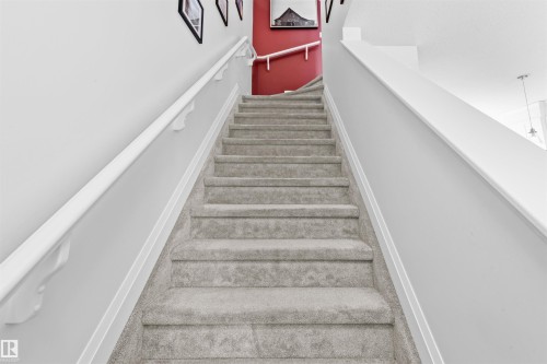 Carpeted staircase featuring light gray carpeting, white painted handrails, and a contrasting accent wall with framed artwork - 389 Charlesworth Drive, Edmonton, AB 