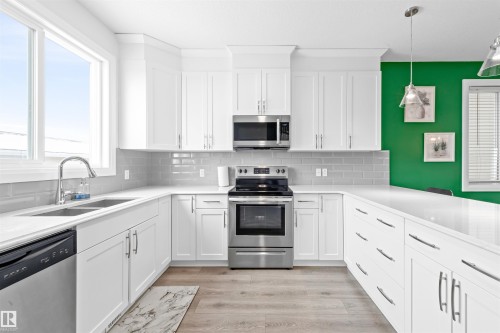 Bright kitchen featuring white shaker-style cabinetry, stainless steel appliances, a double basin sink, light wood-finish flooring, and a subway tile backsplash - 389 Charlesworth Drive, Edmonton, AB 