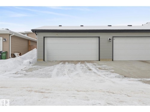 Dual garage doors with exterior wall lighting, concrete driveway, and siding facade - 389 Charlesworth Drive, Edmonton, AB 