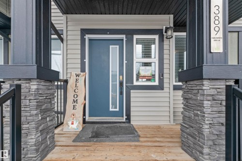 Inviting front entry featuring a blue door with a vertical glass insert, framed by siding and stone-clad pillars - 389 Charlesworth Drive, Edmonton, AB 