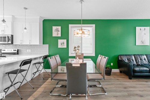Open-concept kitchen and dining area featuring wood-finish flooring, a kitchen island with seating, white shaker cabinetry, and stainless steel appliances including a microwave and range - 389 Charlesworth Drive, Edmonton, AB 