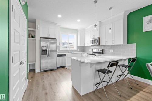 Modern kitchen featuring white cabinetry, stainless steel appliances, light wood-finish flooring, a white countertop island, and a subway tile backsplash - 389 Charlesworth Drive, Edmonton, AB 