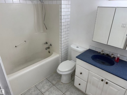 Bathroom featuring a white tub-shower combination, subway tile surround, white toilet, and a vanity with a blue countertop and white cabinetry - 14537 121 Street, Edmonton, AB 