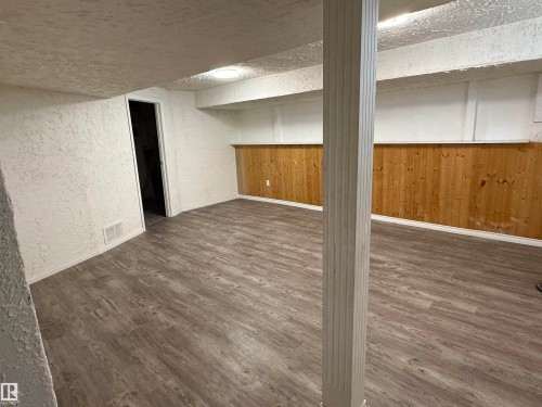 Spacious room featuring wood-finish flooring, white textured walls, and natural wood paneling - 14537 121 Street, Edmonton, AB 