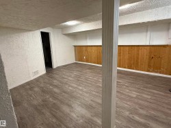 Spacious room featuring wood-finish flooring, white textured walls, and natural wood paneling - 