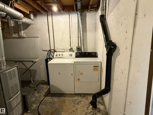 Dedicated laundry area featuring a white washing machine, matching dryer, exposed overhead joists, and utility piping - 14537 121 Street, Edmonton, AB 