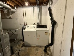 Dedicated laundry area featuring a white washing machine, matching dryer, exposed overhead joists, and utility piping - 