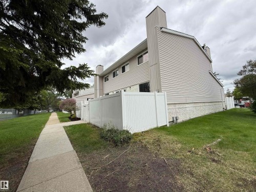 Townhome exterior featuring light-colored siding, a white privacy fence, and a concrete sidewalk - 14537 121 Street, Edmonton, AB 