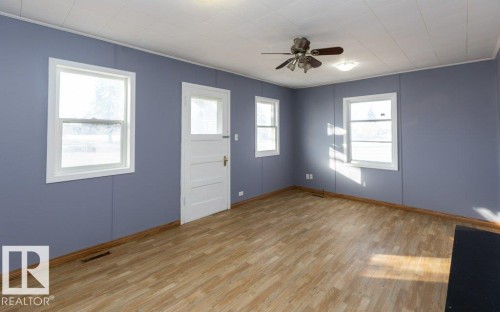 Room featuring wood-finish flooring, two windows with white trim, a multi-pane door, and a ceiling fan with integrated lighting - 9836 100 Street, Westlock, AB 