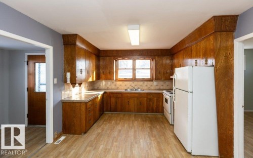 Kitchen featuring extensive wood-finish cabinetry, light-toned countertops, and a tile backsplash - 9836 100 Street, Westlock, AB 