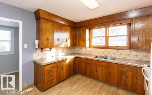 Kitchen featuring extensive wood cabinetry, laminate countertops, dual-basin stainless steel sink, tiled backsplash, and wood-finish flooring - 9836 100 Street, Westlock, AB 
