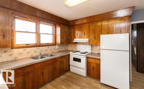 Kitchen featuring wood cabinetry, laminate countertops, a double basin stainless steel sink, and tile backsplash - 9836 100 Street, Westlock, AB 