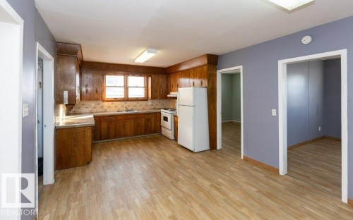 Kitchen featuring wood cabinetry, white appliances, light-toned countertops, a tile backsplash, and wood-finish flooring - 9836 100 Street, Westlock, AB 