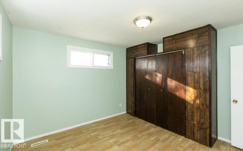 Bedroom featuring wood-finish flooring, light green walls, a white window frame, and built-in wood-paneled wardrobes with integrated overhead storage - 9836 100 Street, Westlock, AB 