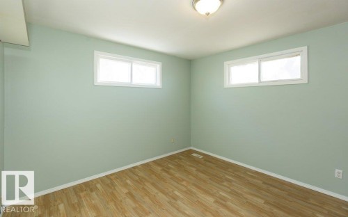 Room featuring two windows with white trim, light green walls, wood-finish flooring, and a flush mount ceiling light fixture - 9836 100 Street, Westlock, AB 