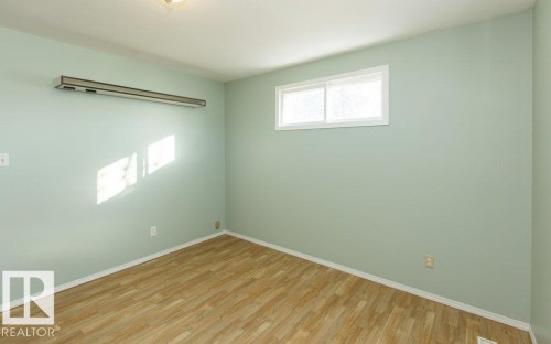 Room featuring light green walls, wood-finish flooring, a white trim window, and a wall-mounted light fixture - 9836 100 Street, Westlock, AB 