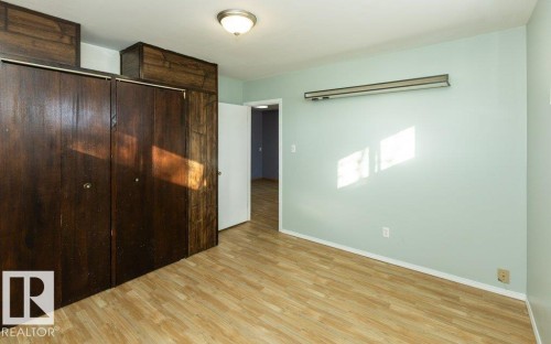 Light wood-finish flooring complemented by a ceiling-mounted light fixture, and walls painted in a soft green hue - 9836 100 Street, Westlock, AB 