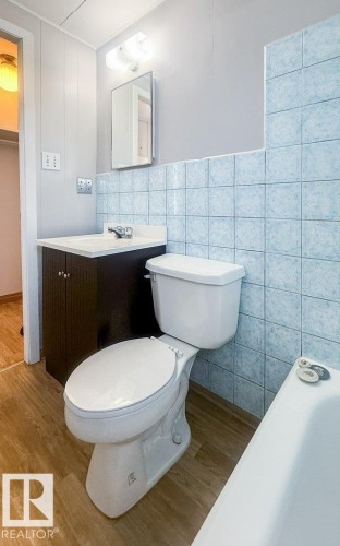 Bathroom featuring light blue wall tiles, wood-finish flooring, a vanity with a dark wood-finish cabinet and white countertop, and a white toilet - 9836 100 Street, Westlock, AB 