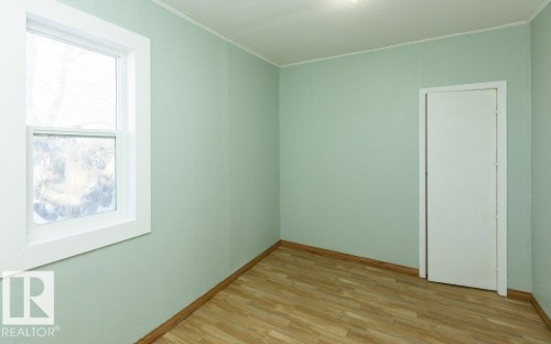 Room featuring light green walls, wood-finish flooring, a white trim window, a white door, and a ceiling-mounted light fixture - 9836 100 Street, Westlock, AB 